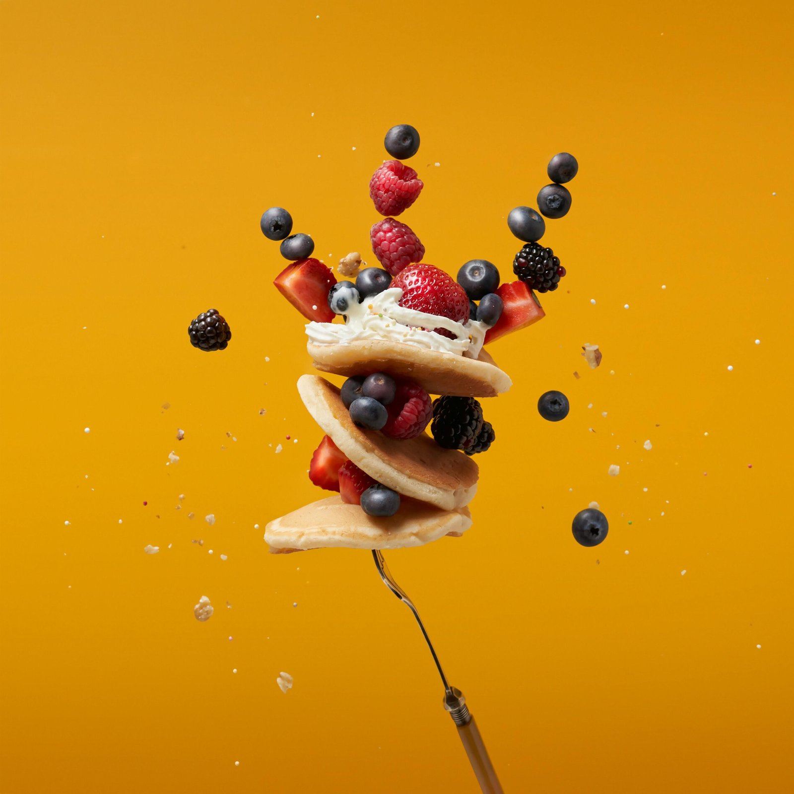 Floating pancakes with fresh berries against a vibrant orange backdrop.