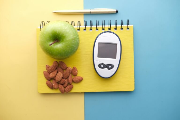Flat lay of diabetes tools, green apple, almonds, and notebook for health planning.