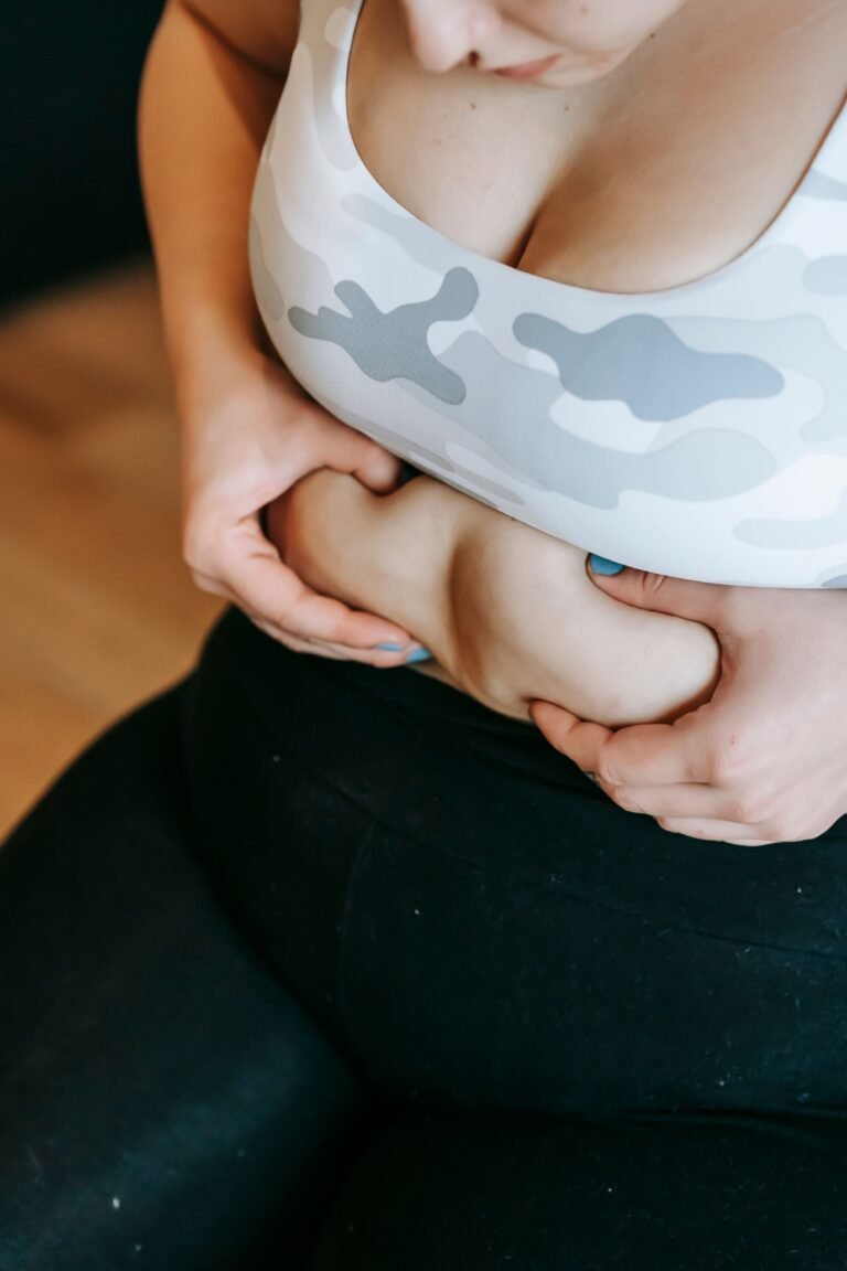 From above of crop unrecognizable plus size female in sportswear touching belly during weight loss workout in gym