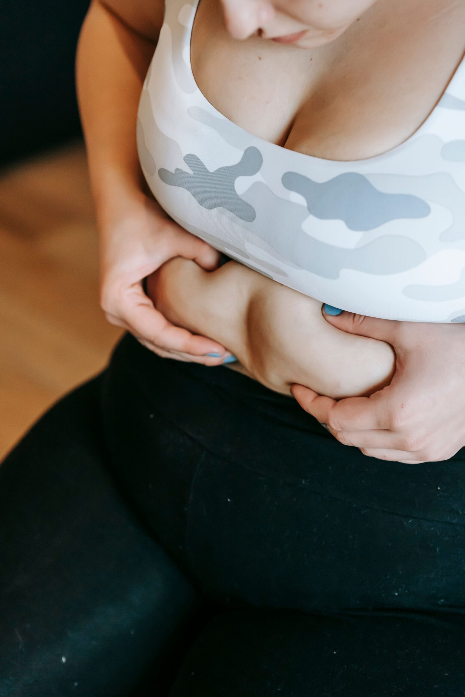 From above of crop unrecognizable plus size female in sportswear touching belly during weight loss workout in gym