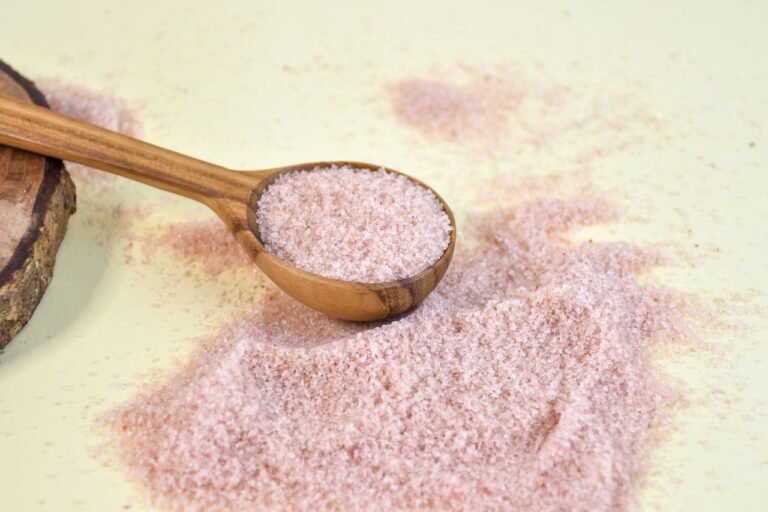 Close-up of pink Himalayan salt in a wooden spoon on a yellow background, highlighting texture.